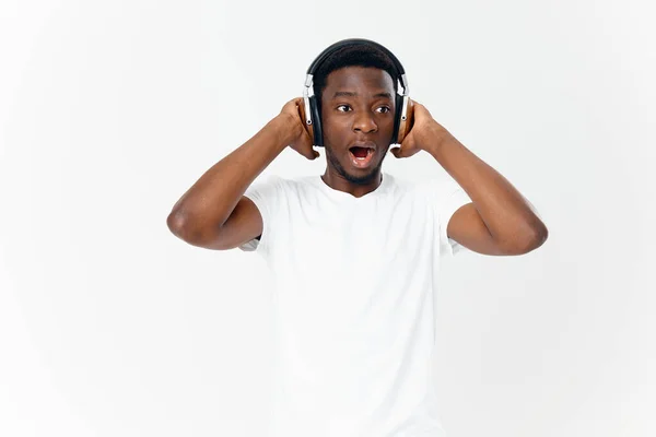 Afrika kökenli bir adam kulaklıkla beyaz bir tişörtle müzik dinliyor. — Stok fotoğraf