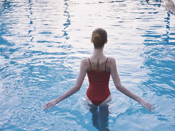 Mulher em um maiô vermelho corre as mãos em água transparente na piscina — Fotografia de Stock