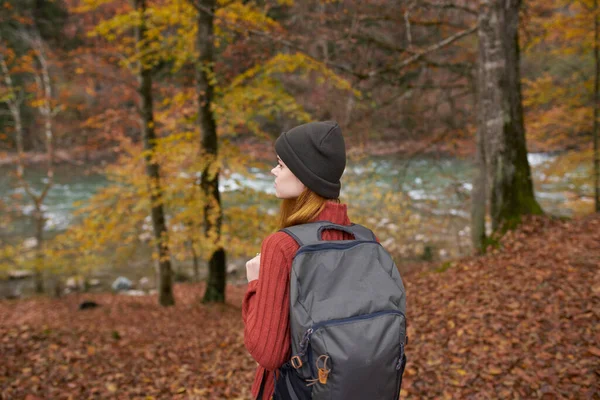 Voyageur avec un sac à dos et dans un chapeau gris dans la forêt d'automne feuilles tombées arbres rivière modèle — Photo
