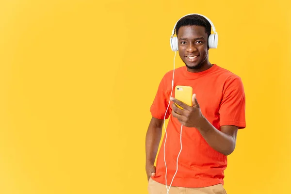 Joyeux Afro-Américain avec un téléphone dans ses mains dans les écouteurs écoute de la musique fond jaune mode — Photo