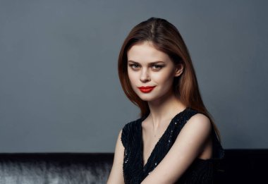 Güzel bir kadın, siyah elbisesiyle koltukta oturmuş, lüks içinde poz veriyor.