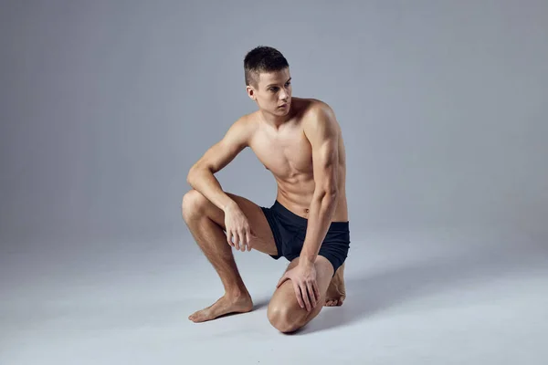 Esportivo homem com corpo muscular em shorts pretos isolado fundo agachamento — Fotografia de Stock
