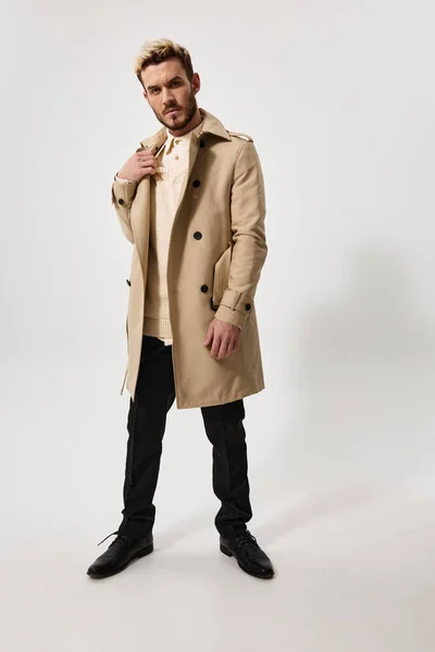 Bel homme blond en manteau beige sur un fond clair et pantalon chaussures costume — Photo