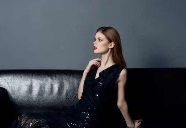 Hermosa mujer en vestido negro sentado en el sofá posando glamour interior — Foto de Stock