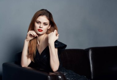 Siyah elbiseli çekici bir kadın kanepede oturup gülümsüyor.