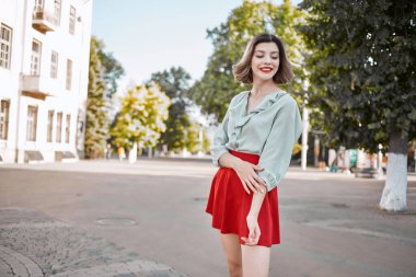 Şehir meydanında kırmızı etekli neşeli bir kadın yürüyor.