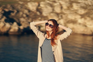 Gezgin, deniz kenarındaki dağlarda tatilde. Elleri kırpık bir manzarayla el kol geziyor.