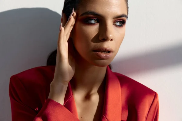 Mujer en una chaqueta roja sostiene una mano cerca de la cara en un estilo de moda de fondo claro —  Fotos de Stock