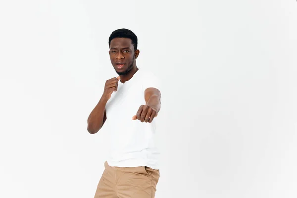 Um homem de aparência africana em uma camiseta branca segura as mãos na frente dele em punhos — Fotografia de Stock