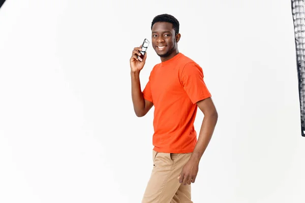 Homme d'apparence africaine avec un téléphone portable sur fond clair et un t-shirt orange — Photo