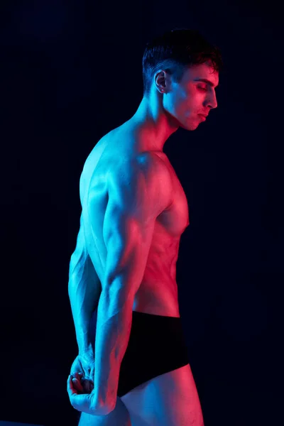 Atletische kerel met atletische bouwen op een zwarte achtergrond zijaanzicht neon licht — Stockfoto