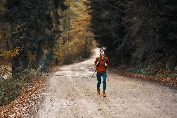 Mujer enérgica corriendo a lo largo de la carretera con mochila en el bosque de otoño — Foto de Stock