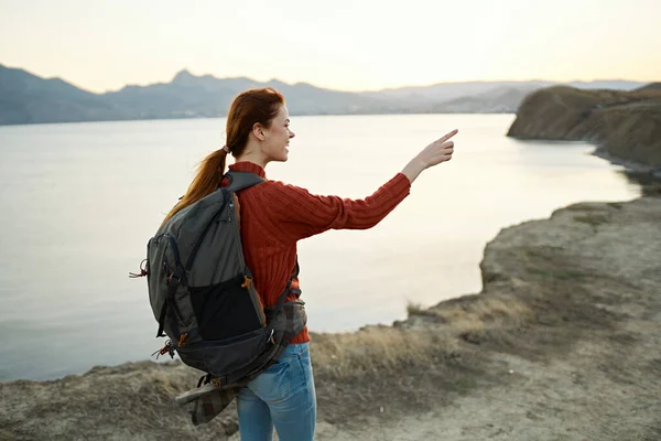 Жінка на заході сонця біля моря в горах з рюкзаком на плечах — стокове фото