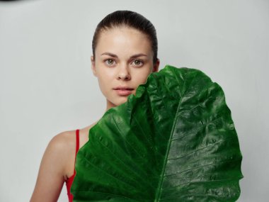 Kırmızı tişörtlü, arka planda yeşil yaprak tutan bir kadın. 