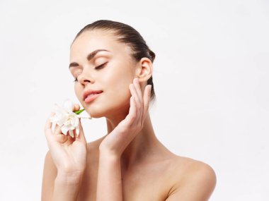 Çıplak omuzlu bir kadın. Gözleri kapalı. Beyaz çiçek kozmetik cazibesi.