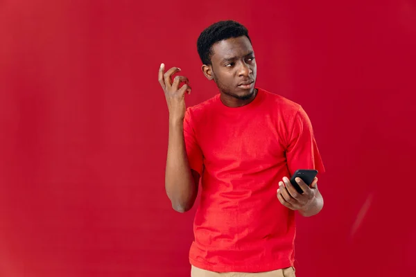 Um homem em uma camiseta vermelha com um telefone em suas mãos comunica tecnologia — Fotografia de Stock