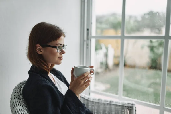 Mulher com óculos sentados em casa perto da janela com uma xícara de café — Fotografia de Stock