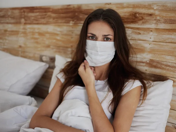 Женщина в медицинской маске лежит в постели в карантинной пандемии коронавируса — стоковое фото