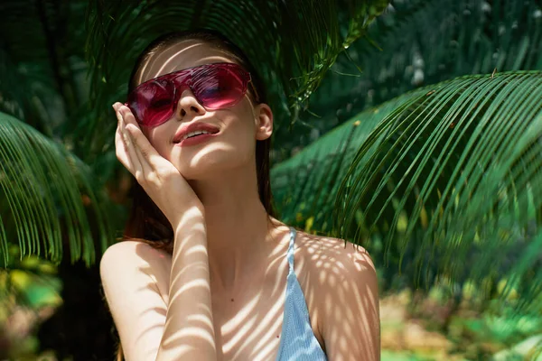 Woman in a swimsuit and sunglasses green leaves exotic sun — Stock Photo, Image