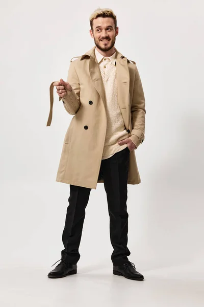 Счастливый человек в бежевом пальто держит руку в кармане и пояс в руке — стоковое фото