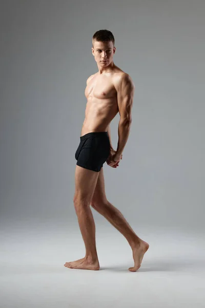 Nackter Mann in schwarzen Höschen auf grauem Hintergrund, aufgepumpte Muskeln des Oberkörpers — Stockfoto