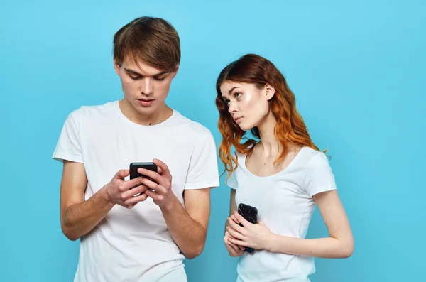 Mann und Frau stehen neben dem Telefon in den Händen Kommunikationstechnologie blauer Hintergrund — Stockfoto