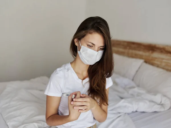 Женщина, сидящая в постели с термометром под рукой, проверяя температуру — стоковое фото