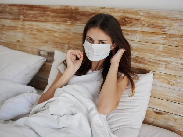 Woman in medical mask lying in bed under the covers and gesturing with her hands cropped view — Stock Photo, Image