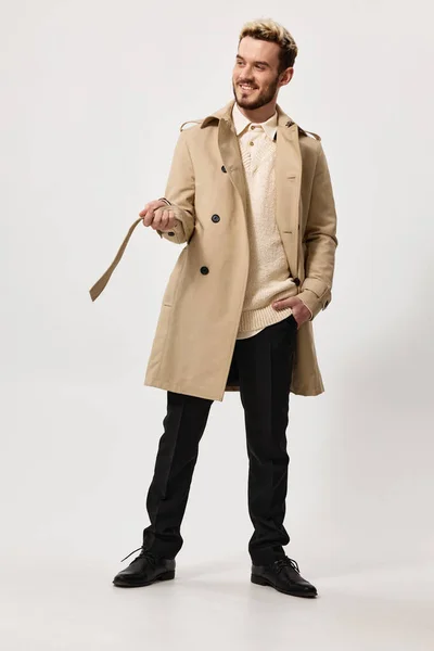 Стильний молодий чоловік в пальто з поясом в руці на світлому фоні — стокове фото