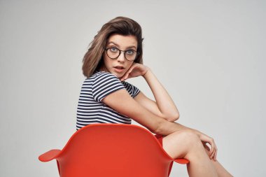 Güzel sarışın kırmızı sandalyede oturmuş gözlüklü moda yapıyor.