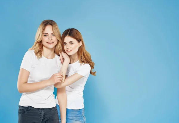 Copines gaies se tiennent l'un à côté de l'autre en blanc t-shirts amitié mode fond bleu — Photo