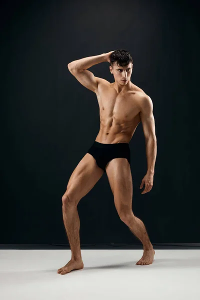 Mann mit aufgepumptem muskulösen Körper in schwarzen Shorts posiert vor dunklem Hintergrund — Stockfoto