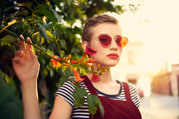 Kvinna i solglasögon står bredvid en buske med blommor i gatan livsstil — Stockfoto