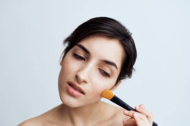 Güzel esmer, çıplak omuzlarına makyaj yapıyor.