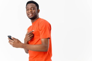  Cep telefonlu, Afrika görünümlü, turuncu tişörtlü, hafif arka planlı bir adam. 