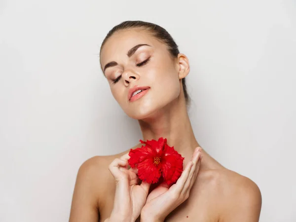 Mujer con los ojos cerrados hombros desnudos flor roja en las manos encanto fondo claro —  Fotos de Stock