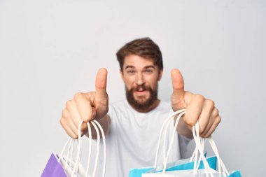 Beyaz tişörtlü sakallı bir adam. Elinde paketler var.