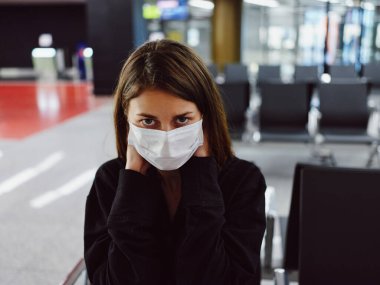 Tıbbi maskeli kadın havaalanında bekliyor.