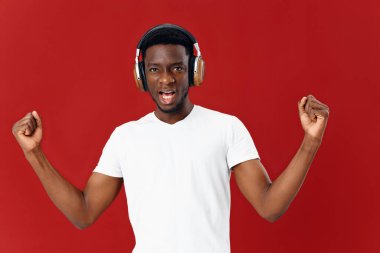 Beyaz tişörtlü, kulaklıklı, el hareketleriyle müzik yapan bir adam.