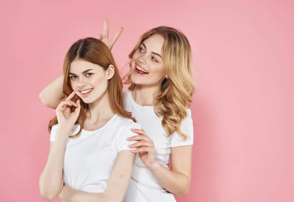 Dos novias en camisetas blancas abraza emociones fondo rosa —  Fotos de Stock