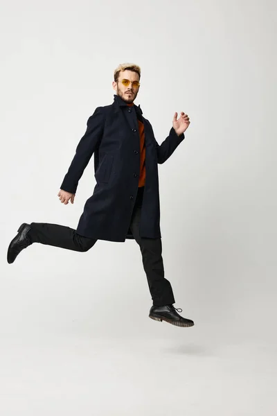 A man in dark trousers and a black coat runs on a light background in full growth — Stock Photo, Image