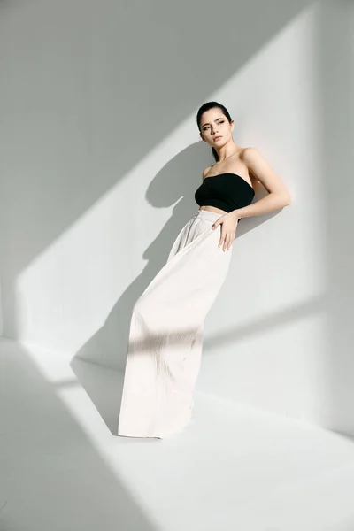 Mujer de moda en camiseta negra y falda blanca apoyada contra la pared en el interior — Foto de Stock