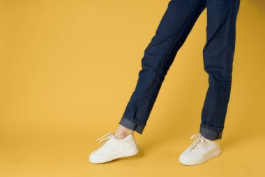 Beyaz spor ayakkabılı kadın bacakları sarı arka plan tarzı poz veriyor.