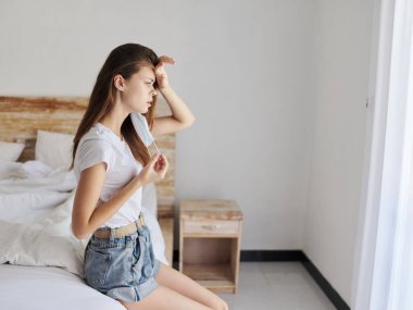 Yüzünde tıbbi maske olan üzgün bir kadın elleriyle kafasına dokunuyor.