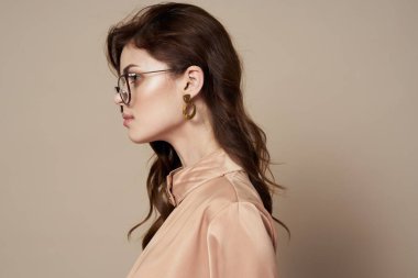 Gözlüklü, güzel, bej gömlekli bir kadın. Lüks, münzevi bir geçmişi var.