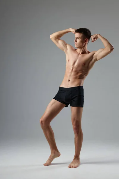 Idrottare i svarta shorts håller händerna bakom huvudet naken bål grå rum full längd — Stockfoto