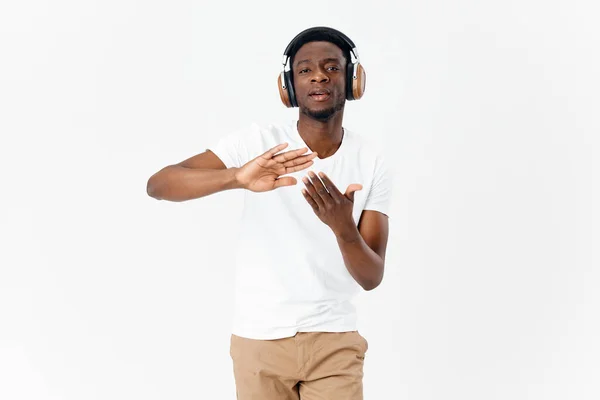 Homme d'apparence africaine dans les écouteurs gesticulant avec ses mains fond de lumière amateur de musique — Photo