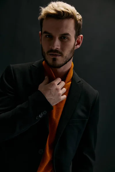 Porträtt av en attraktiv blond man på en mörk bakgrund i en orange tröja och rock — Stockfoto