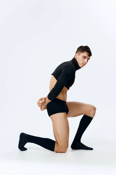 Ein Mann mit athletischem Körperbau steht kniend in einer Pullover-Unterhose und Socken auf einer hellen Hintergrundseite — Stockfoto
