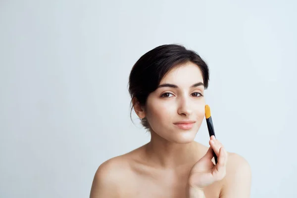 Pretty brunette applying makeup on face close-up naked shoulders — Stock Photo, Image